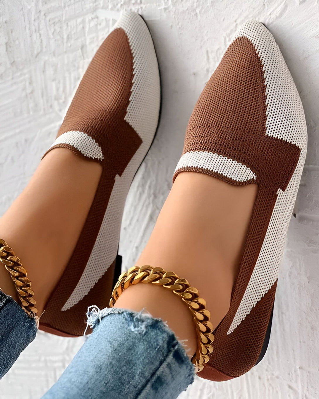 Une femme porte des chaussures marron et blanches avec un motif en maille. Elle porte également un jean bleu et un bracelet de cheville doré.