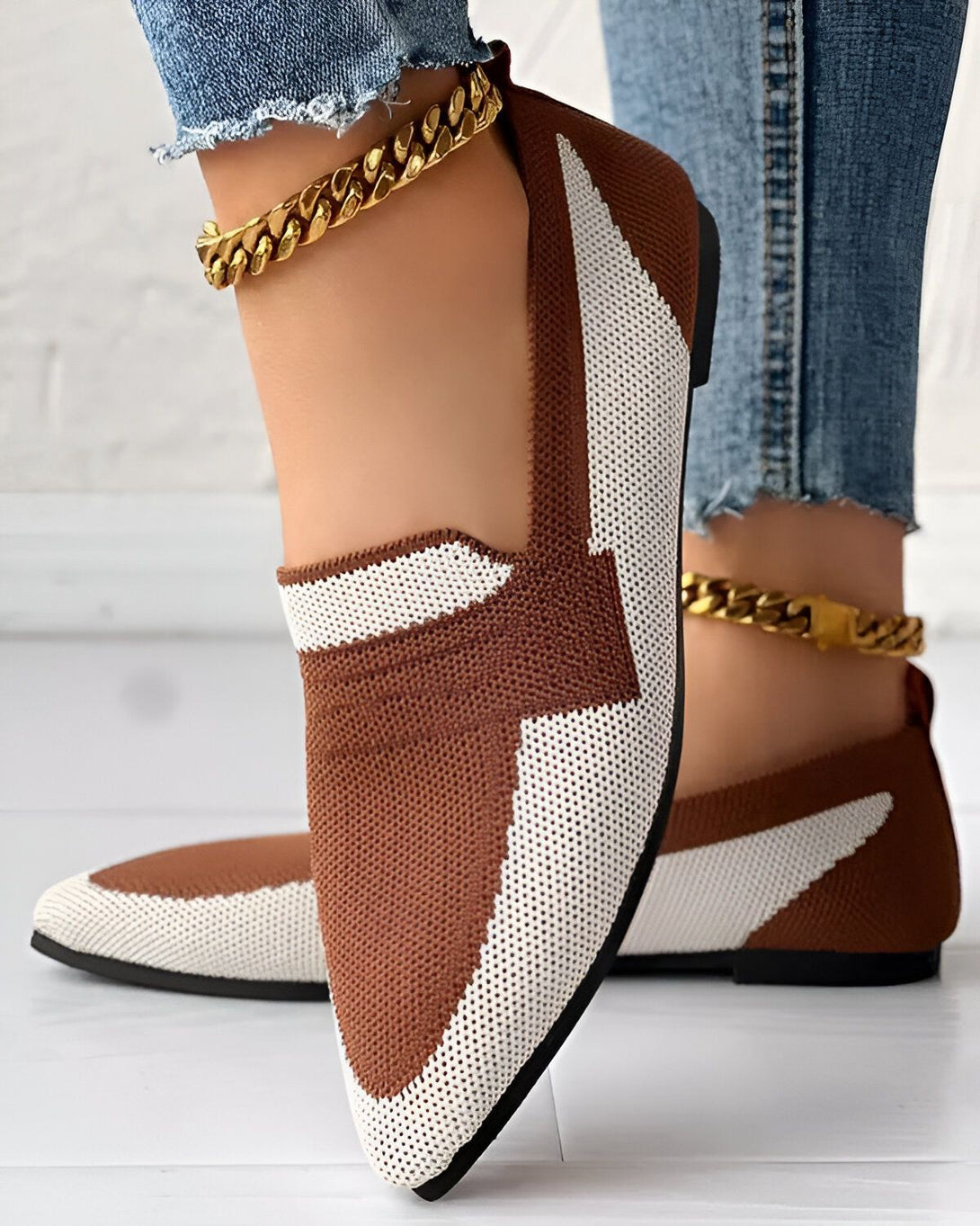 Une image d'une paire de chaussures marron et blanche avec un motif en maille. Les chaussures sont portées par une femme qui porte un jean bleu et des chaussettes blanches. La femme est debout sur un sol en bois.