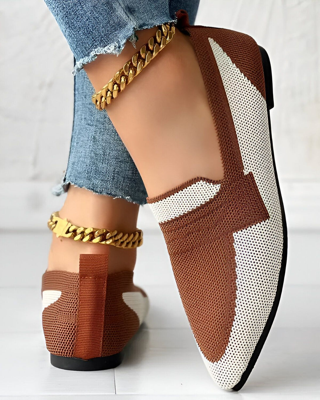 Une femme porte des chaussures marron et blanches avec un jean bleu et des bracelets de cheville en or.