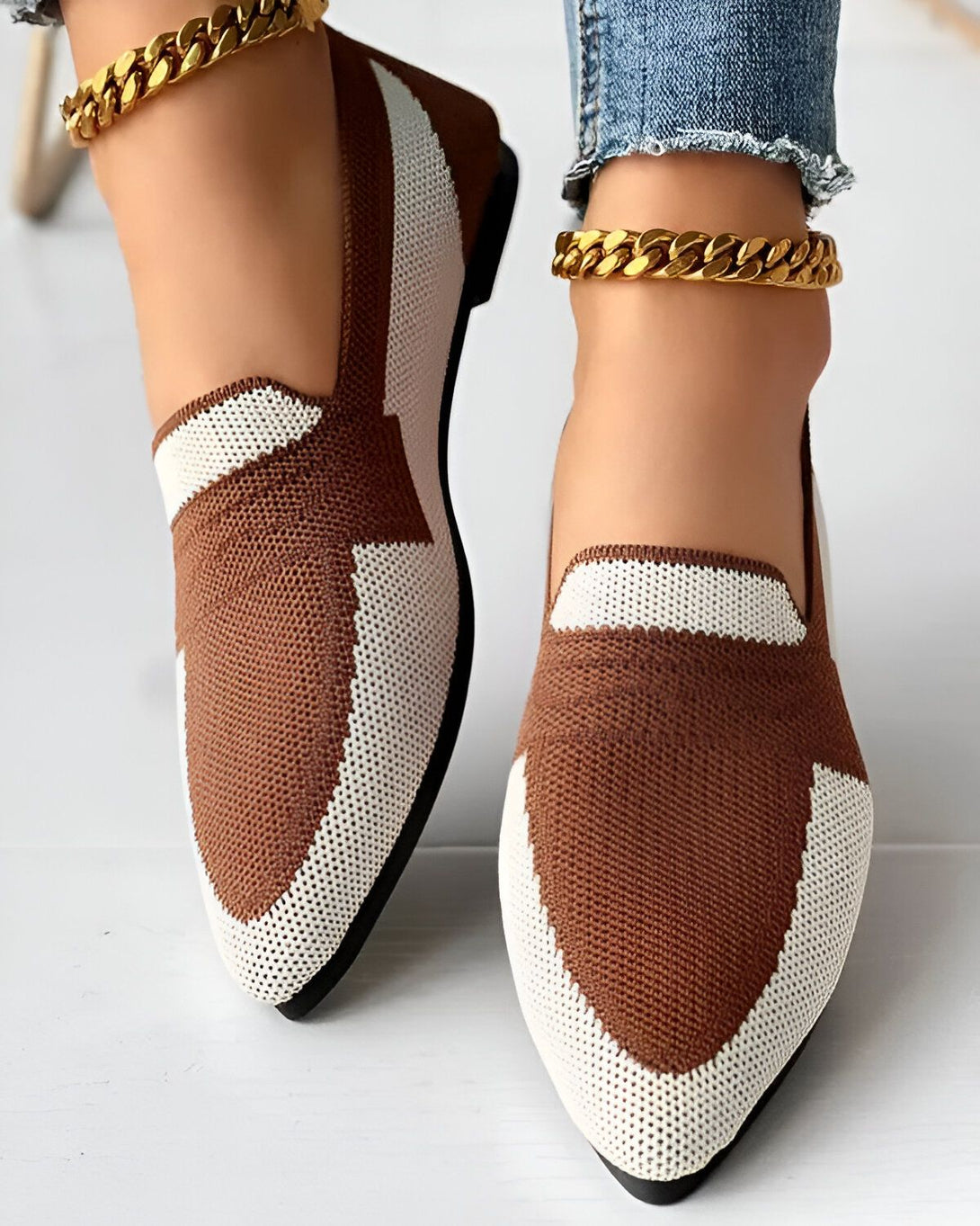 Une image de chaussures marron et blanches avec un bout pointu et une chaîne dorée autour de la cheville.