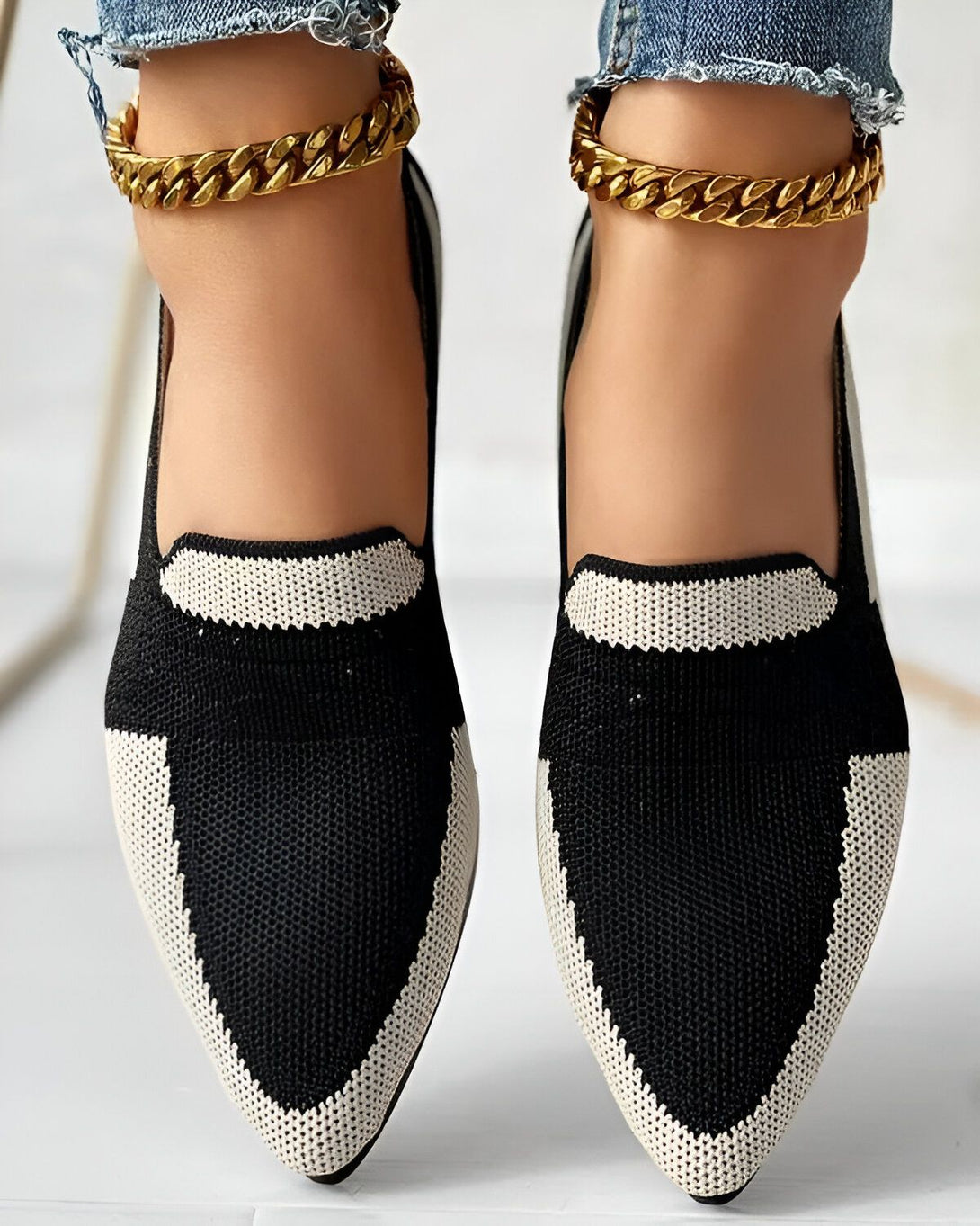 Une femme porte des chaussures noires et blanches à talons avec des chaînes dorées aux chevilles.