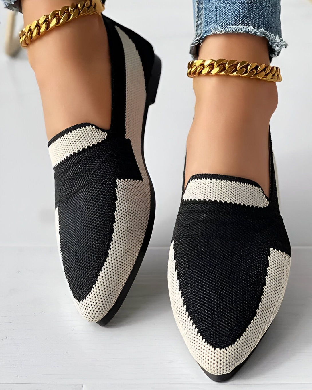 Une image de chaussures plates noires et blanches avec des semelles en caoutchouc. Les chaussures sont portées par une femme qui porte un jean bleu et des chaussettes blanches. La femme est debout sur un sol en bois.