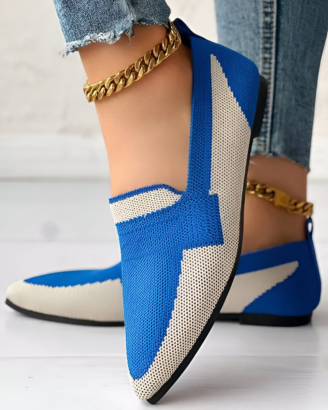 Une femme porte des chaussures bleues et blanches avec un jean et des bijoux en or.
