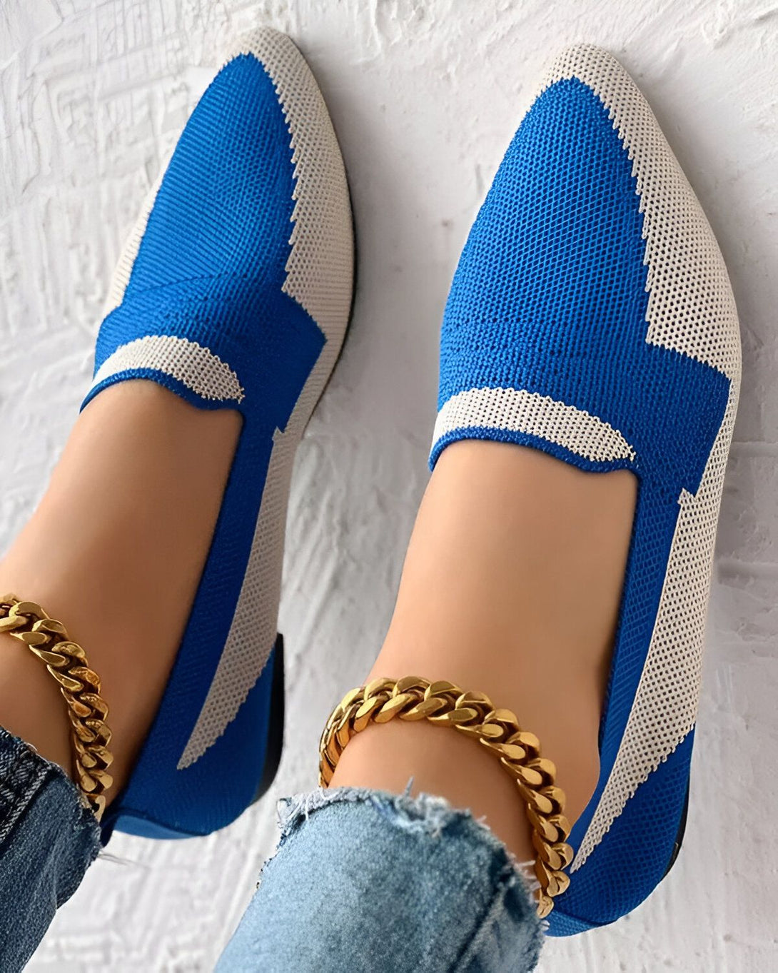 Une image d'une paire de chaussures bleues et blanches. Les chaussures sont en maille et ont un bout pointu. Elles sont portées par une femme qui porte également un jean et une cheville dorée.