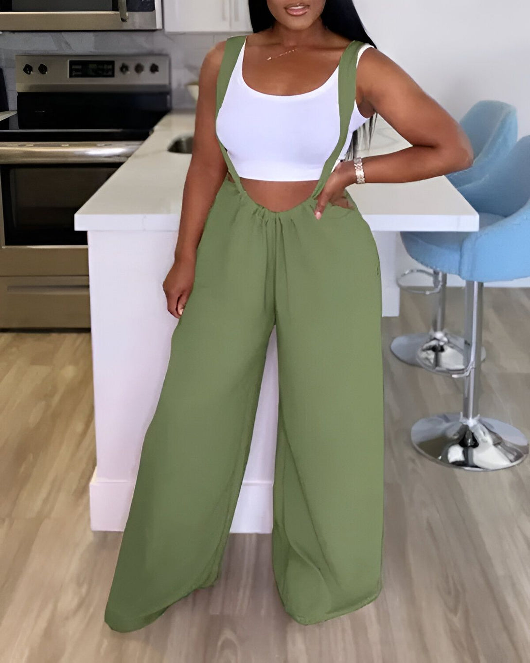 Une femme porte une combinaison pantalon vert olive avec un haut blanc. Elle est dans une cuisine et est debout près d'un comptoir.
