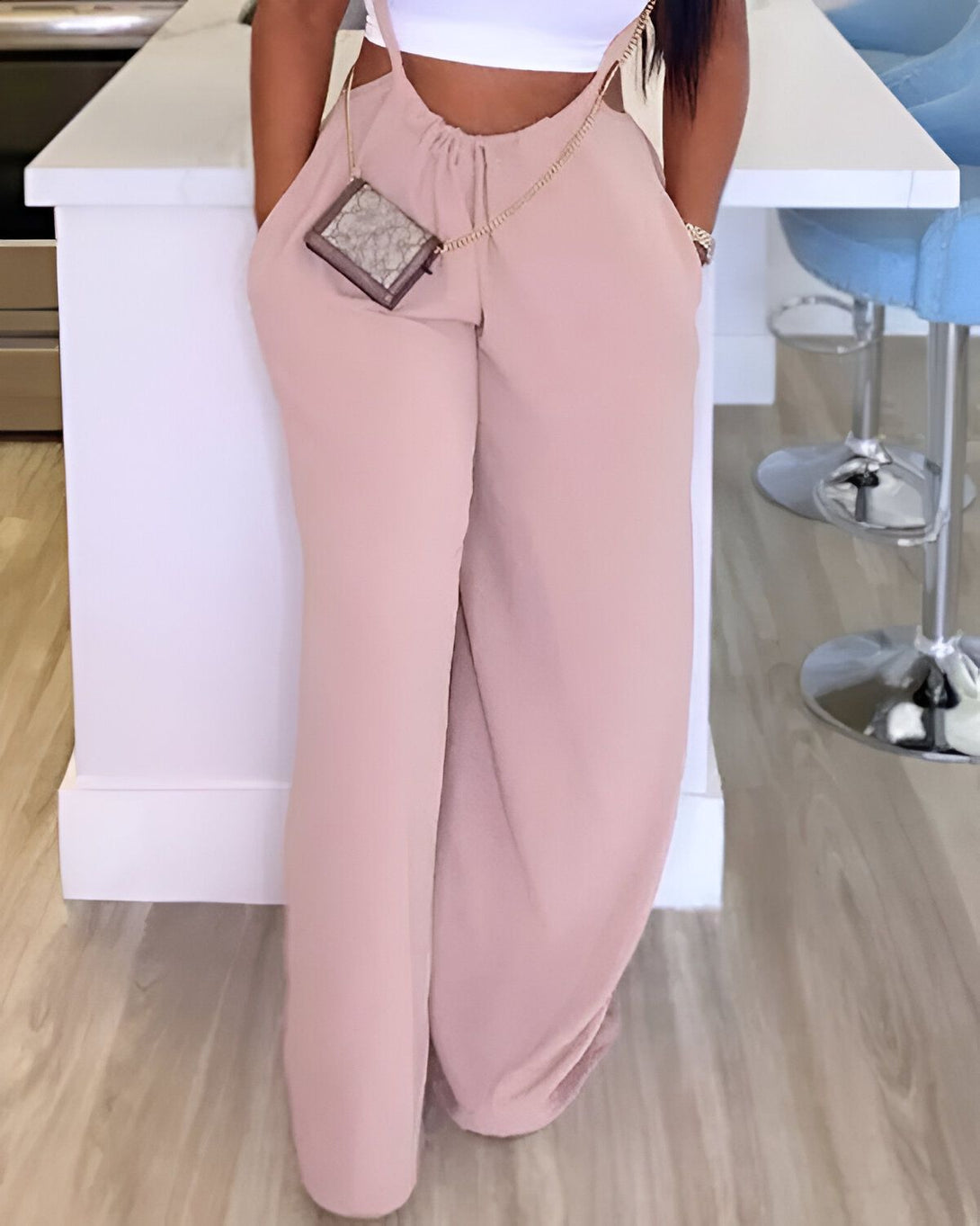 Une femme porte un pantalon beige taille haute et une brassière blanche. Elle a un sac à main marron à la taille.