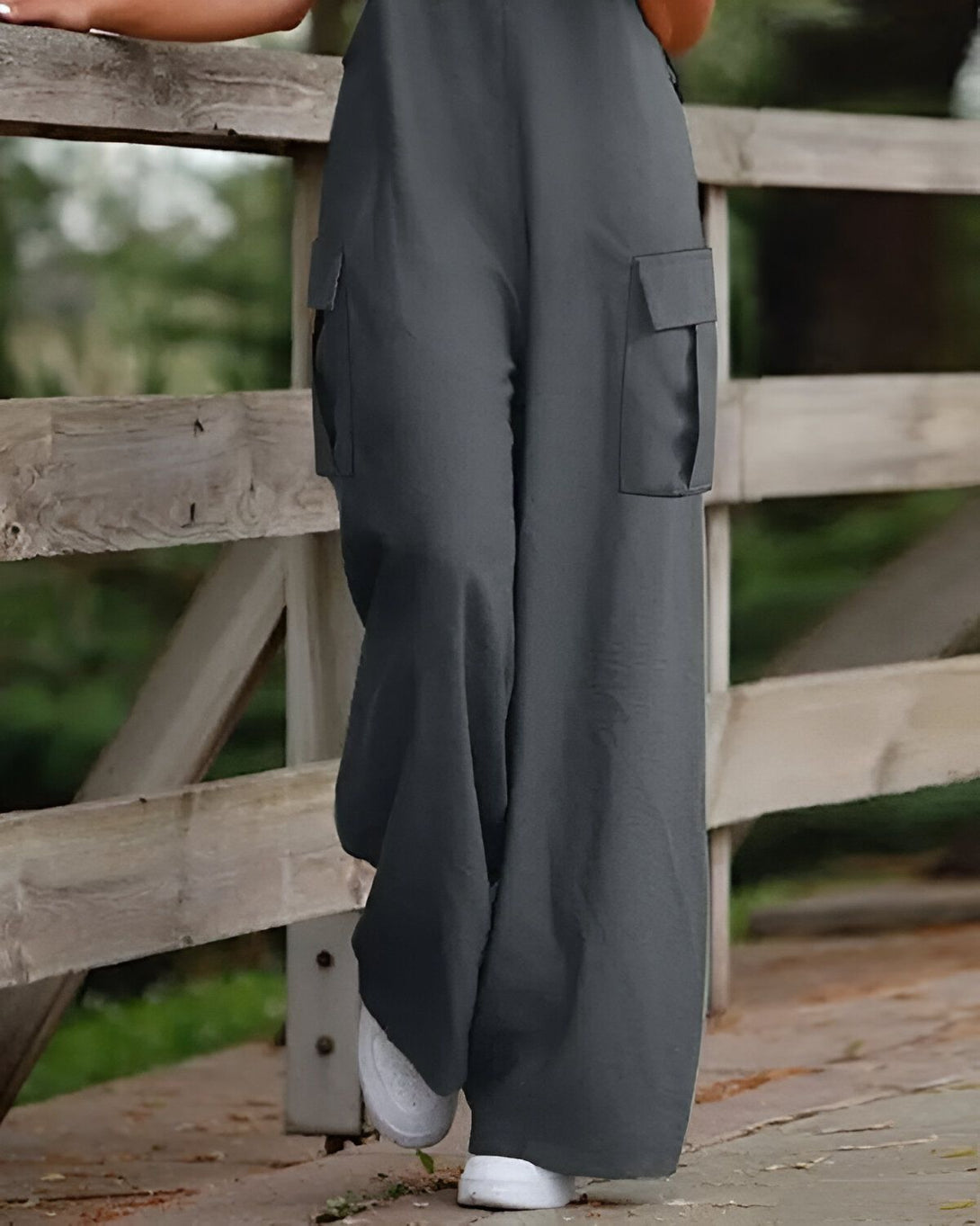 Une femme porte une combinaison-pantalon large et grise. Elle est debout sur un pont en bois et tient le garde-corps.