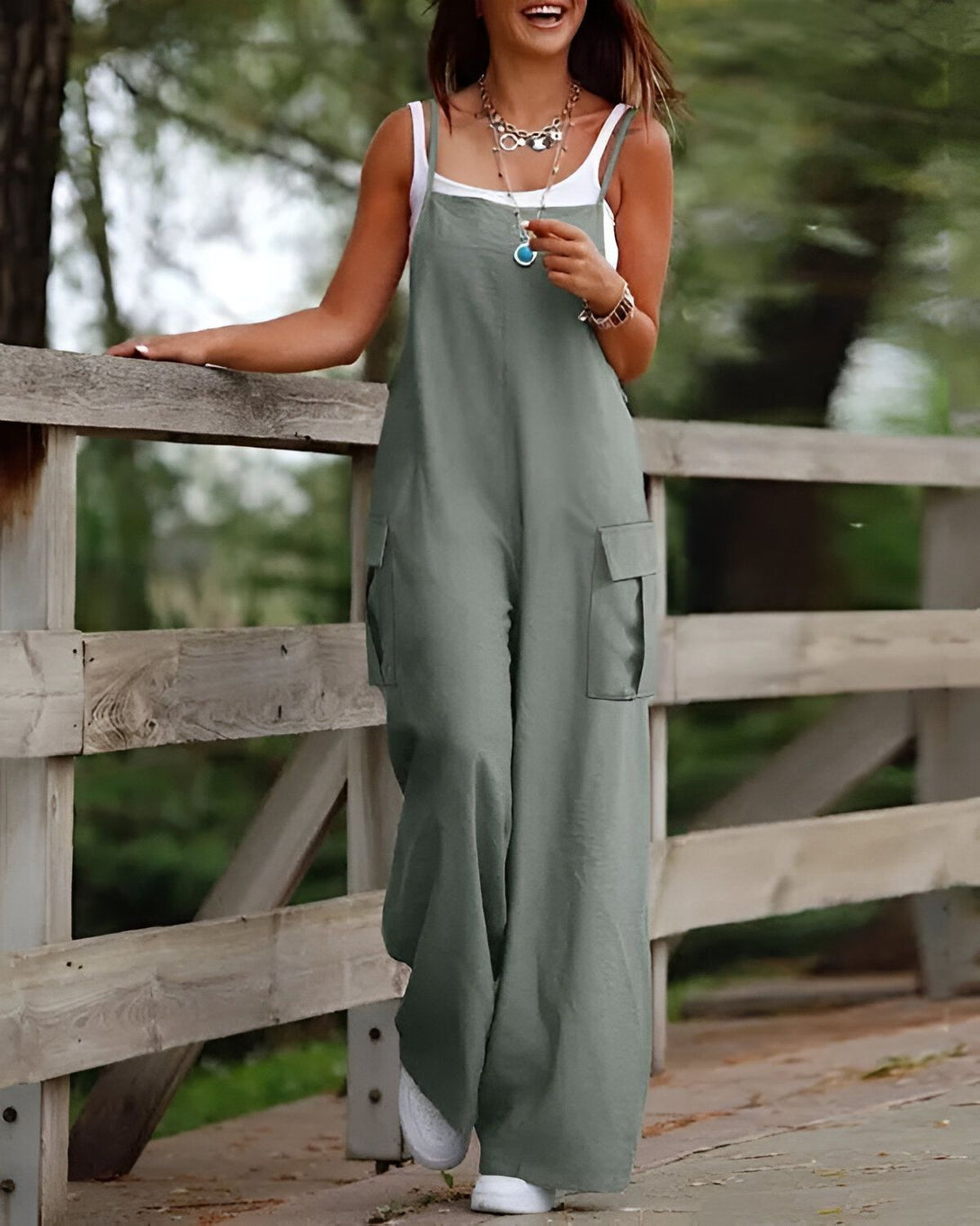 Une femme porte une combinaison-pantalon verte kaki. Elle est debout sur un pont en bois et sourit.