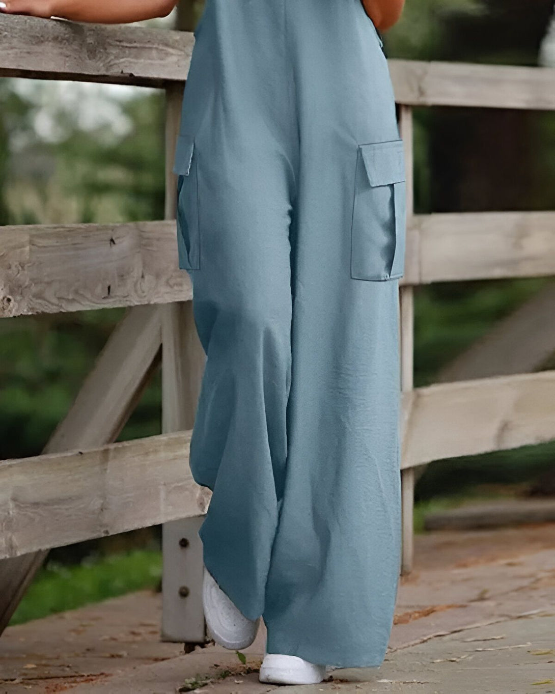 Une femme porte une combinaison-pantalon bleu clair. Elle est debout sur un pont en bois et tient le garde-corps.