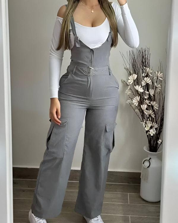 Une femme porte une combinaison pantalon grise avec des poches cargo et un haut blanc. Elle est également chaussée de baskets blanches.