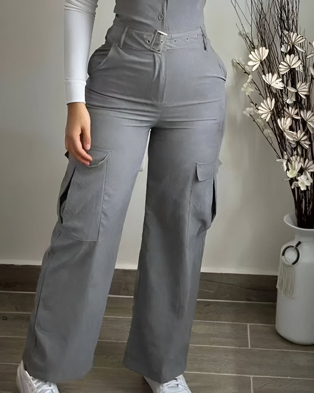Une femme porte un pantalon cargo gris taille haute avec des poches sur les côtés. Elle porte également un haut blanc et des baskets blanches.