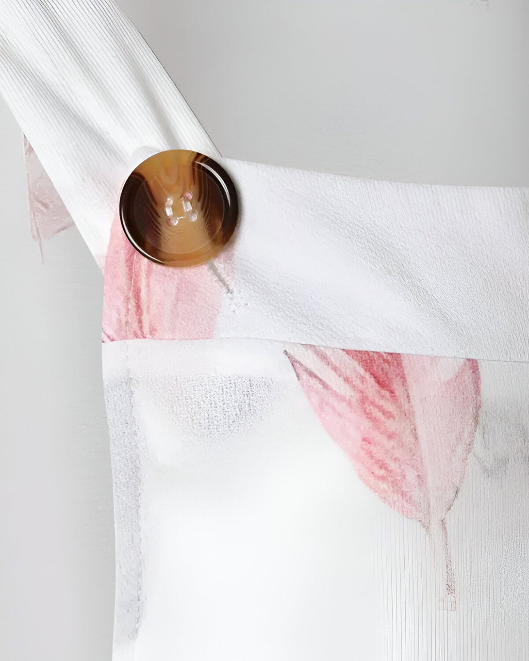 gros plan sur un bouton marron sur une bretelle de vêtement blanc à motif floral rose