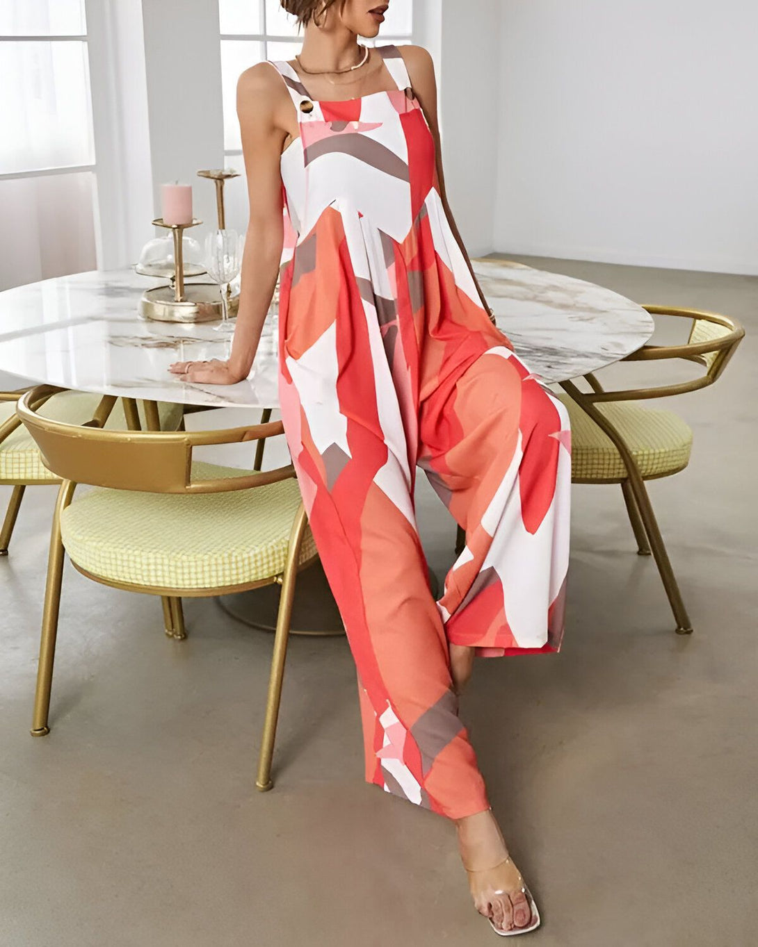 Une femme porte une combinaison pantalon ample et colorée. Elle est debout dans une salle à manger, appuyée sur une table.