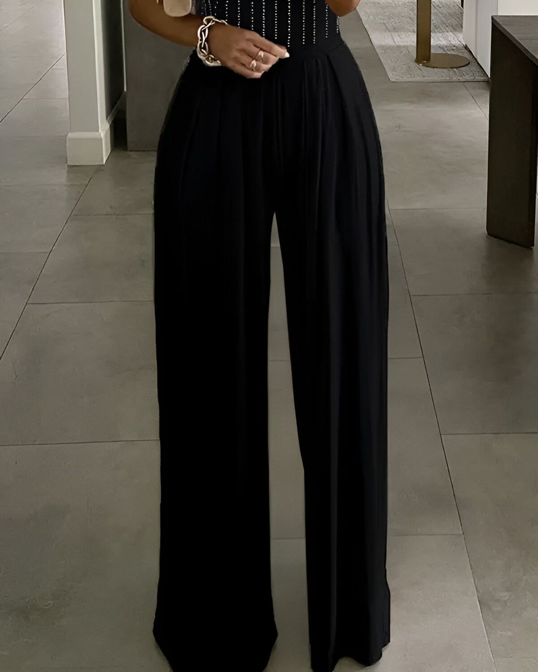 Une femme porte un pantalon large noir taille haute. Le pantalon est ample et fluide, et il est parfait pour une soirée ou une occasion spéciale.