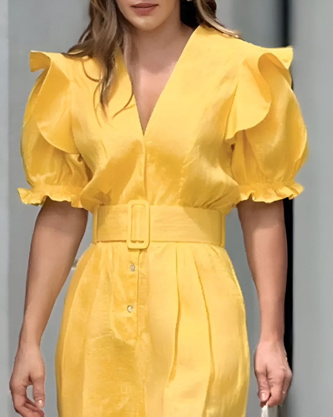 Une femme porte une robe jaune avec des manches bouffantes et une ceinture.