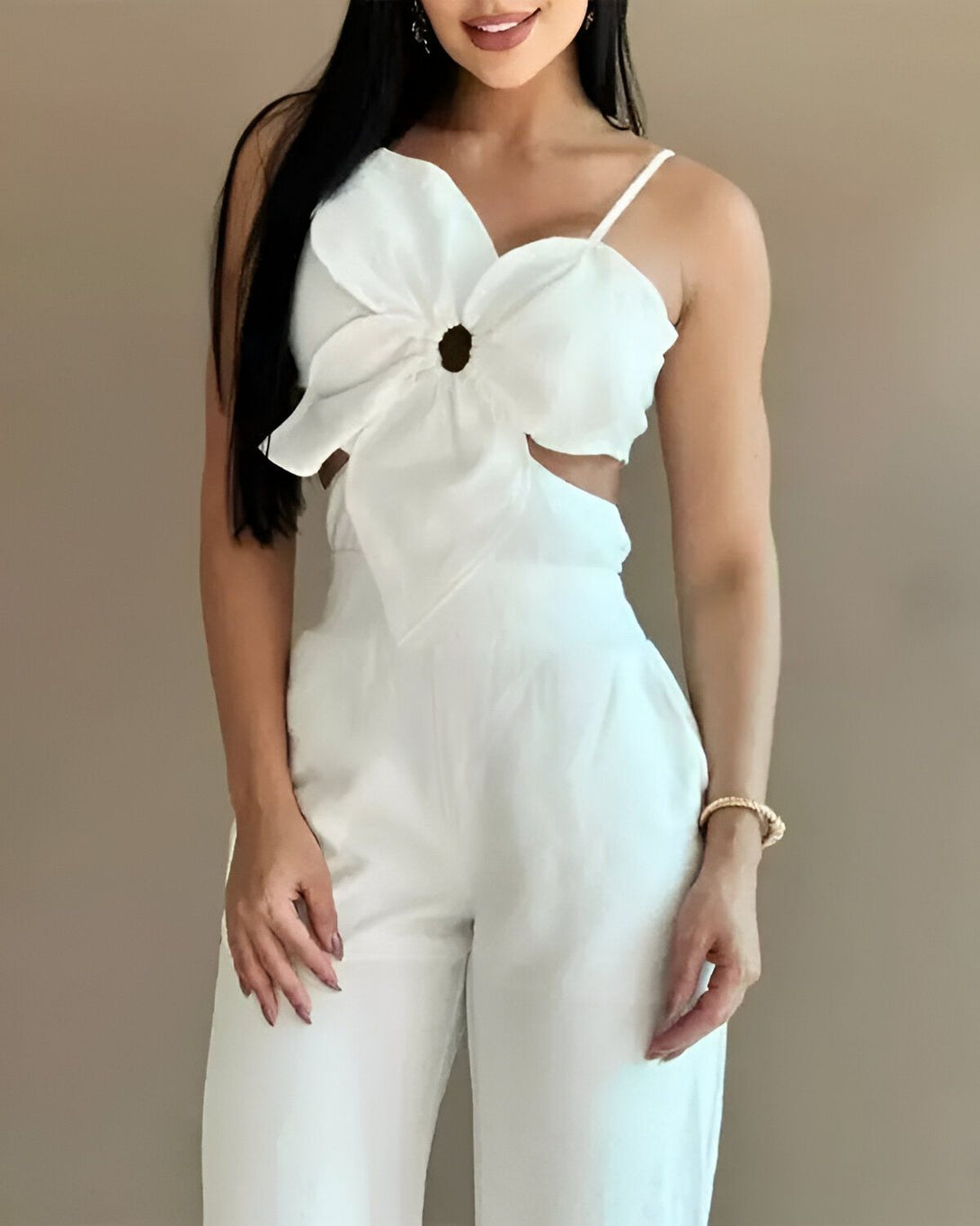 Une femme porte une combinaison pantalon blanche. La combinaison a un décolleté en forme de fleur avec un anneau au milieu.