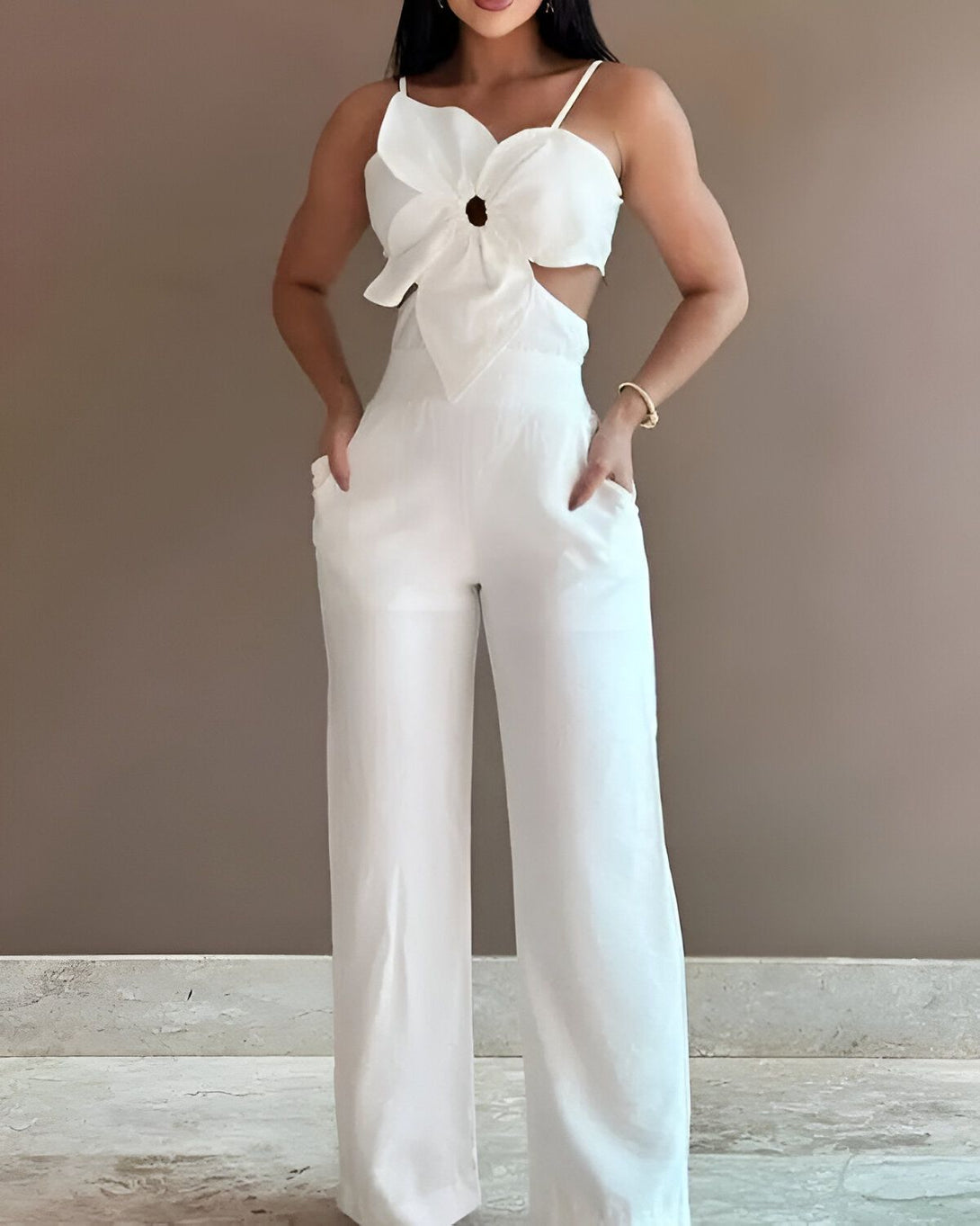 Une femme porte une combinaison pantalon blanche. La combinaison a une découpe en forme de fleur au niveau du buste.