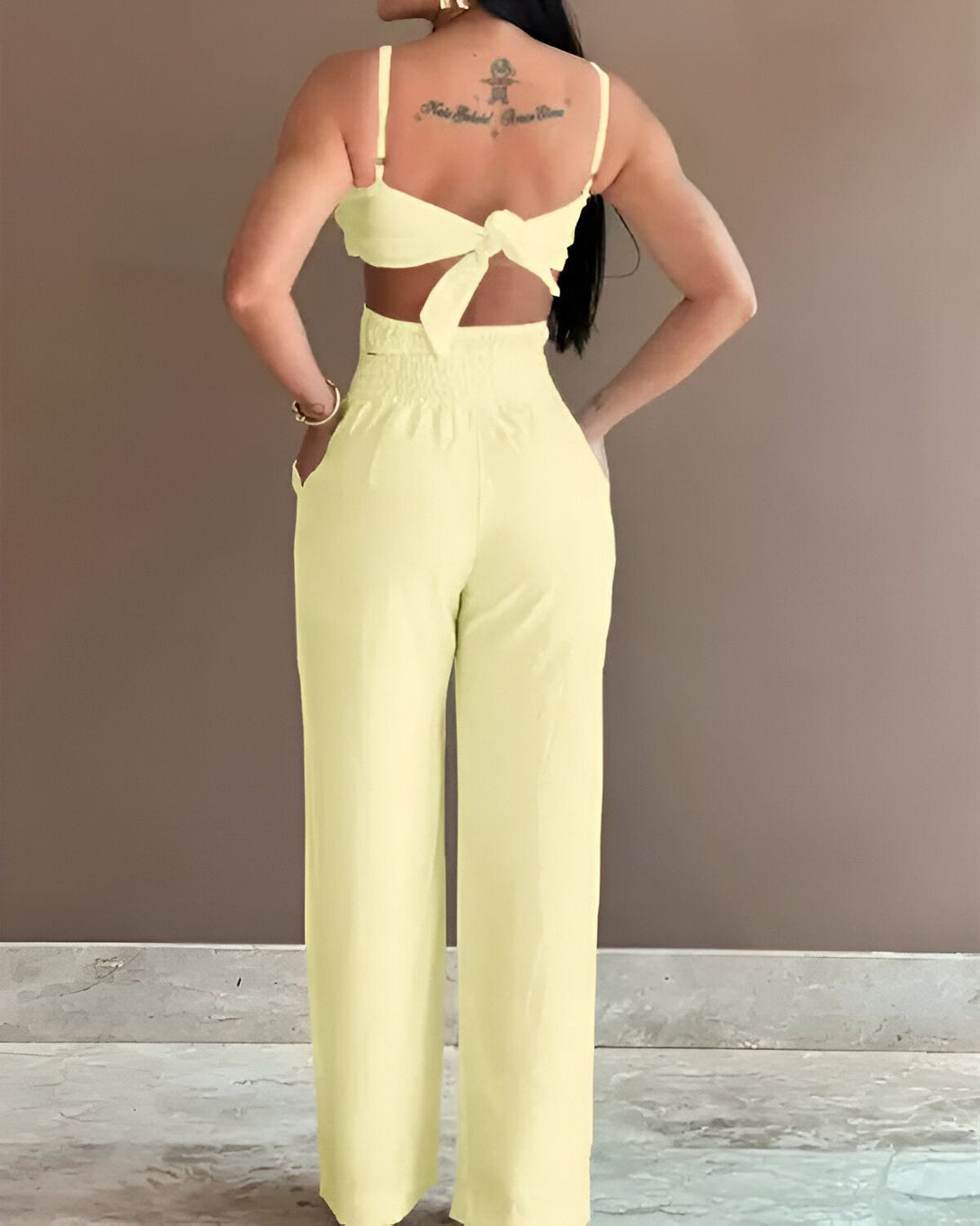 Une femme porte un ensemble pantalon et haut jaune dos nu. Le haut est court et noué dans le dos. Le pantalon est large et taille haute.
