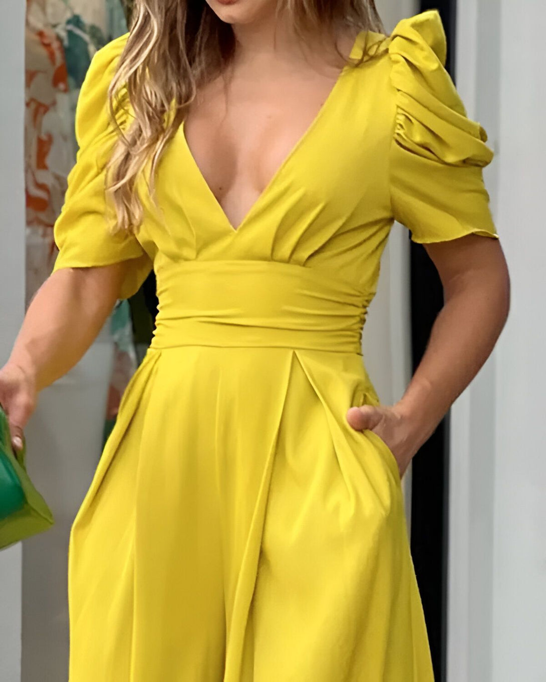 Une femme porte une combinaison-pantalon jaune vif avec un décolleté en V et des manches bouffantes.