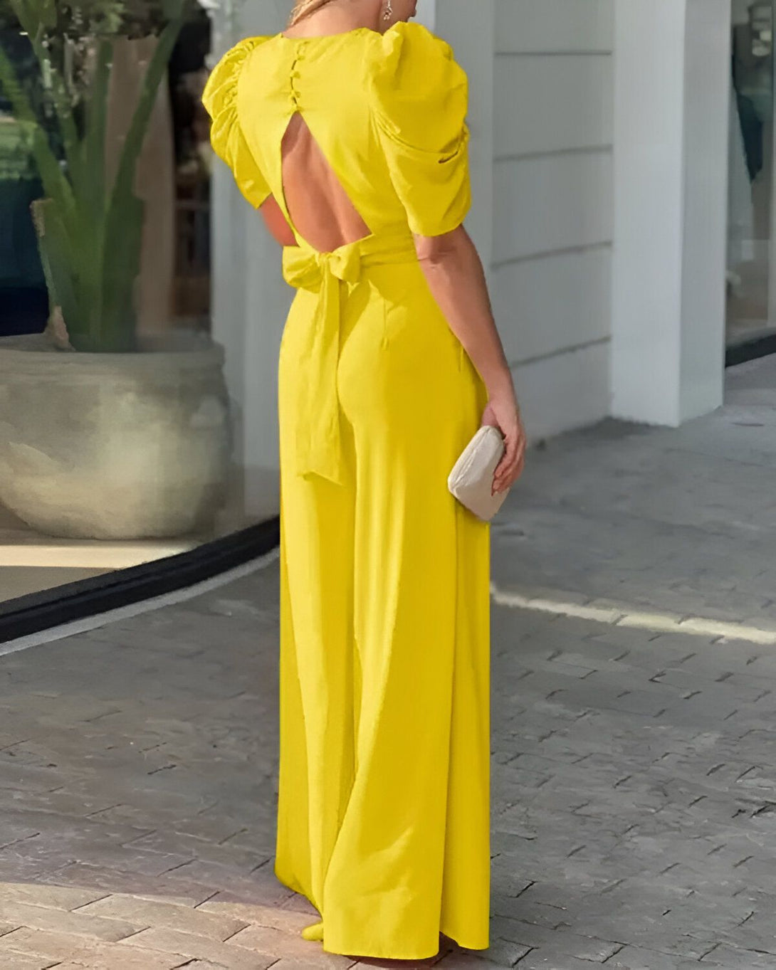 Une femme porte une combinaison-pantalon jaune dos nu avec un nœud à la taille.