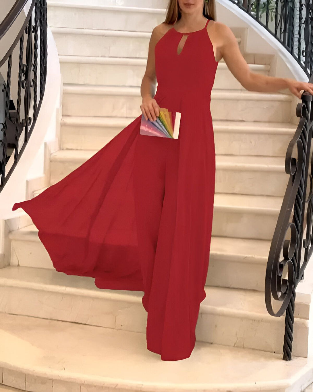 Une femme en robe rouge est debout dans un escalier. Elle porte une pochette arc-en-ciel à la main.