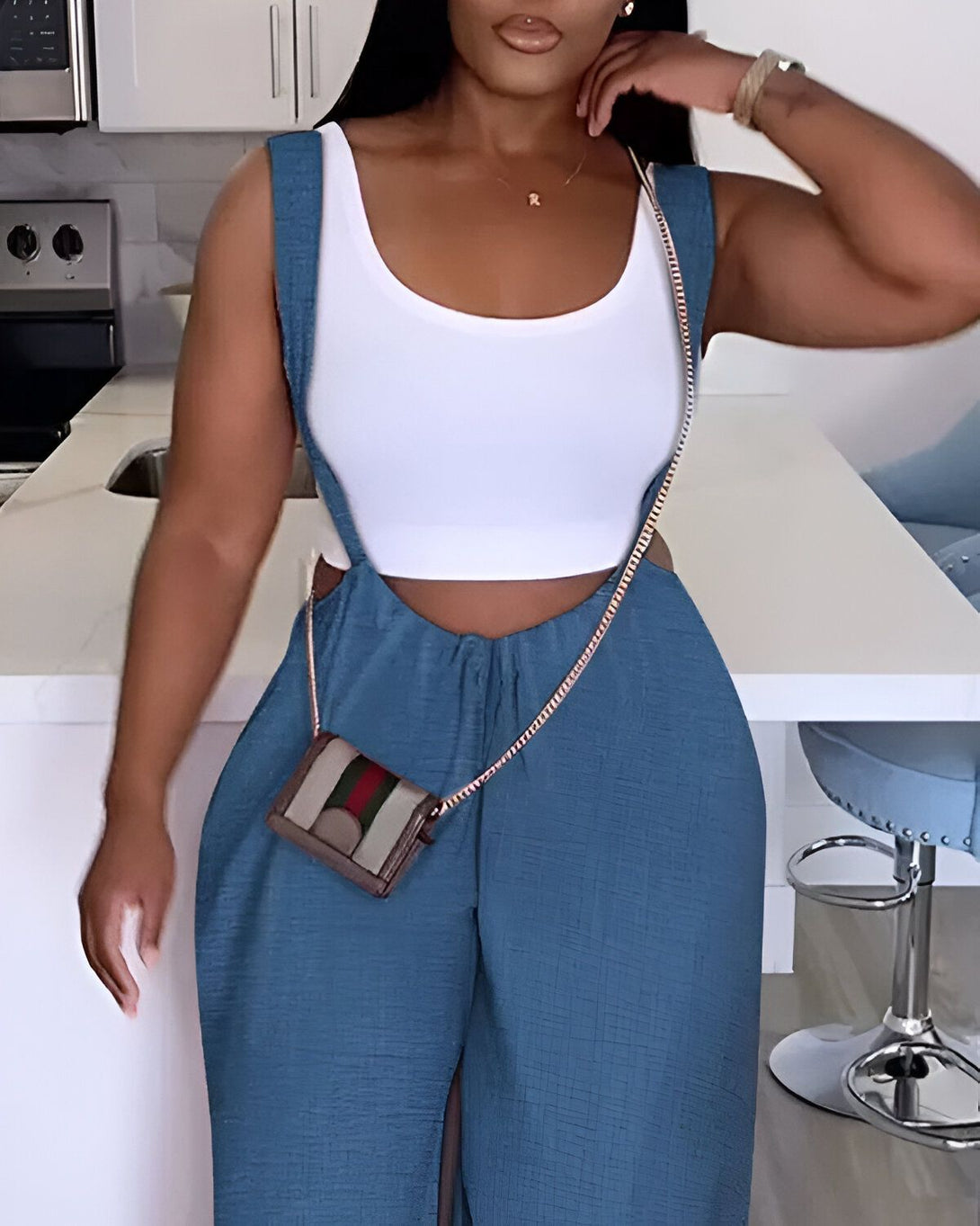 Une femme porte un pantalon bleu sarcelle et un haut blanc. Elle porte également un sac à main marron et des bijoux.