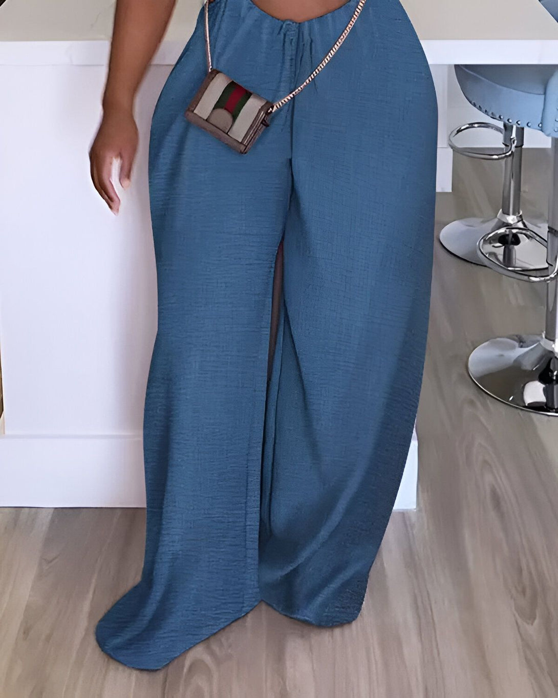 Une femme porte un pantalon bleu large et une brassière assortie. Elle porte également un sac à main marron et des talons hauts.