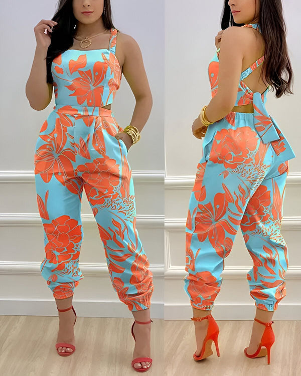 Une femme porte une combinaison pantalon ample à motifs fleuris bleus et oranges. Elle est dos nu et porte des sandales à talons rouges.
