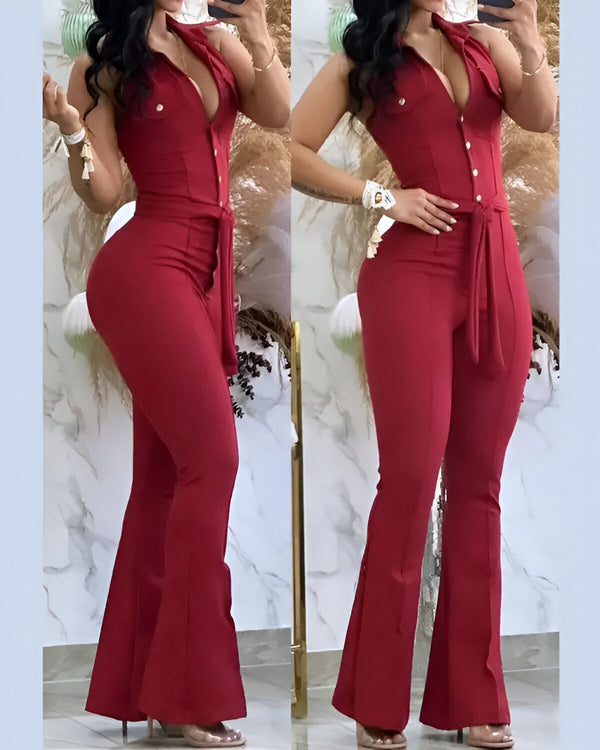 Une femme porte une combinaison rouge avec un décolleté plongeant et des boutons. La combinaison est cintrée à la taille et évasée au niveau des jambes. Elle porte des talons hauts transparents.