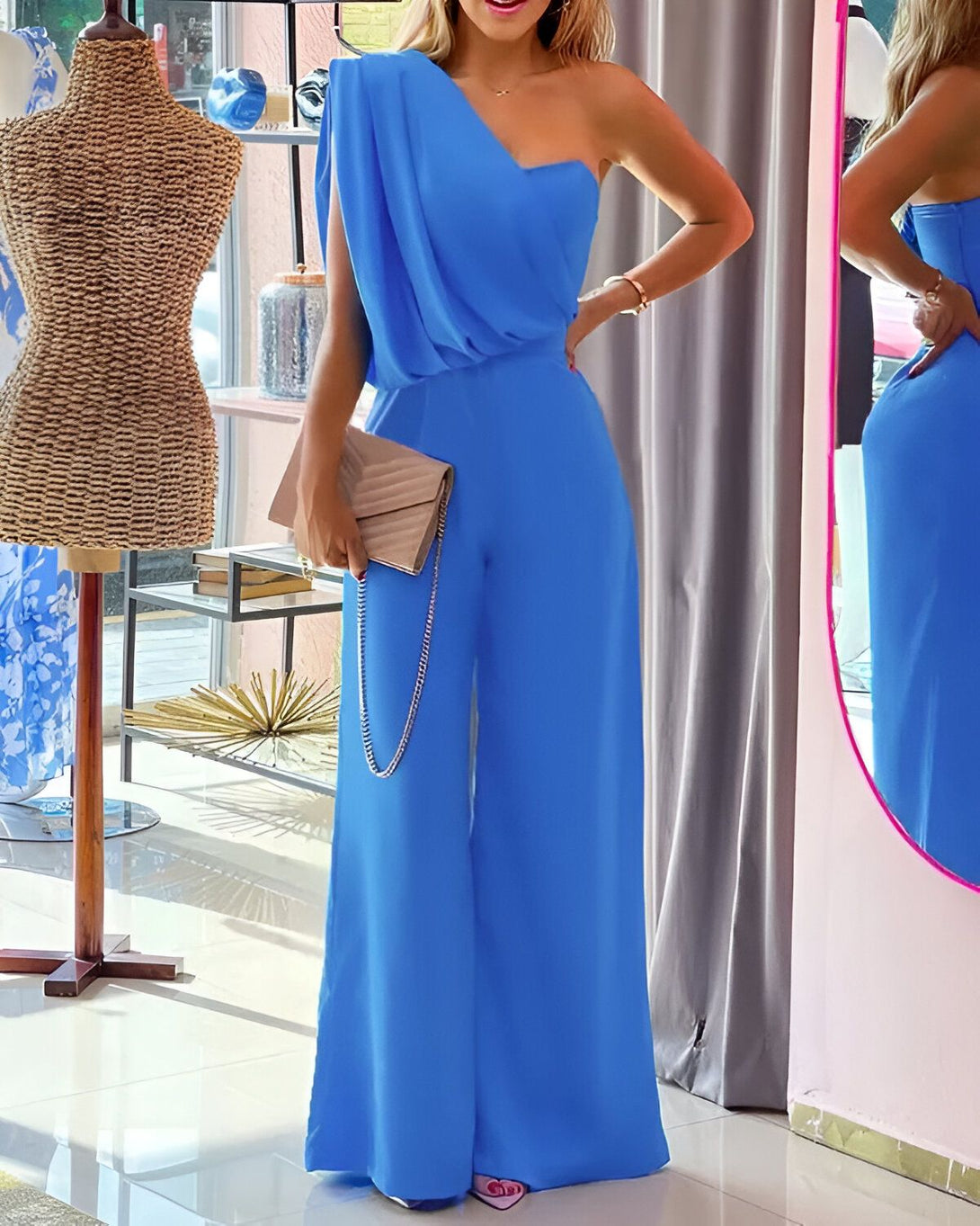 Une femme porte une combinaison pantalon bleu ciel asymétrique. Elle est accessoirisée d'une pochette et de sandales à talons hauts.