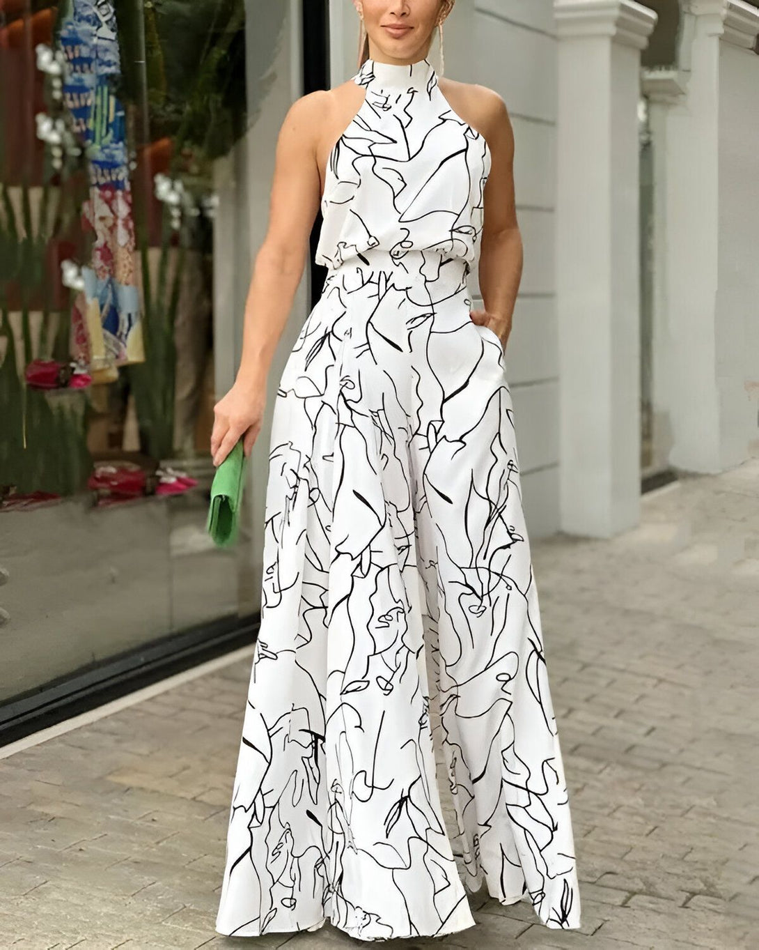 Une femme porte une combinaison pantalon blanche avec un motif de visage noir. Elle porte également un sac à main vert.