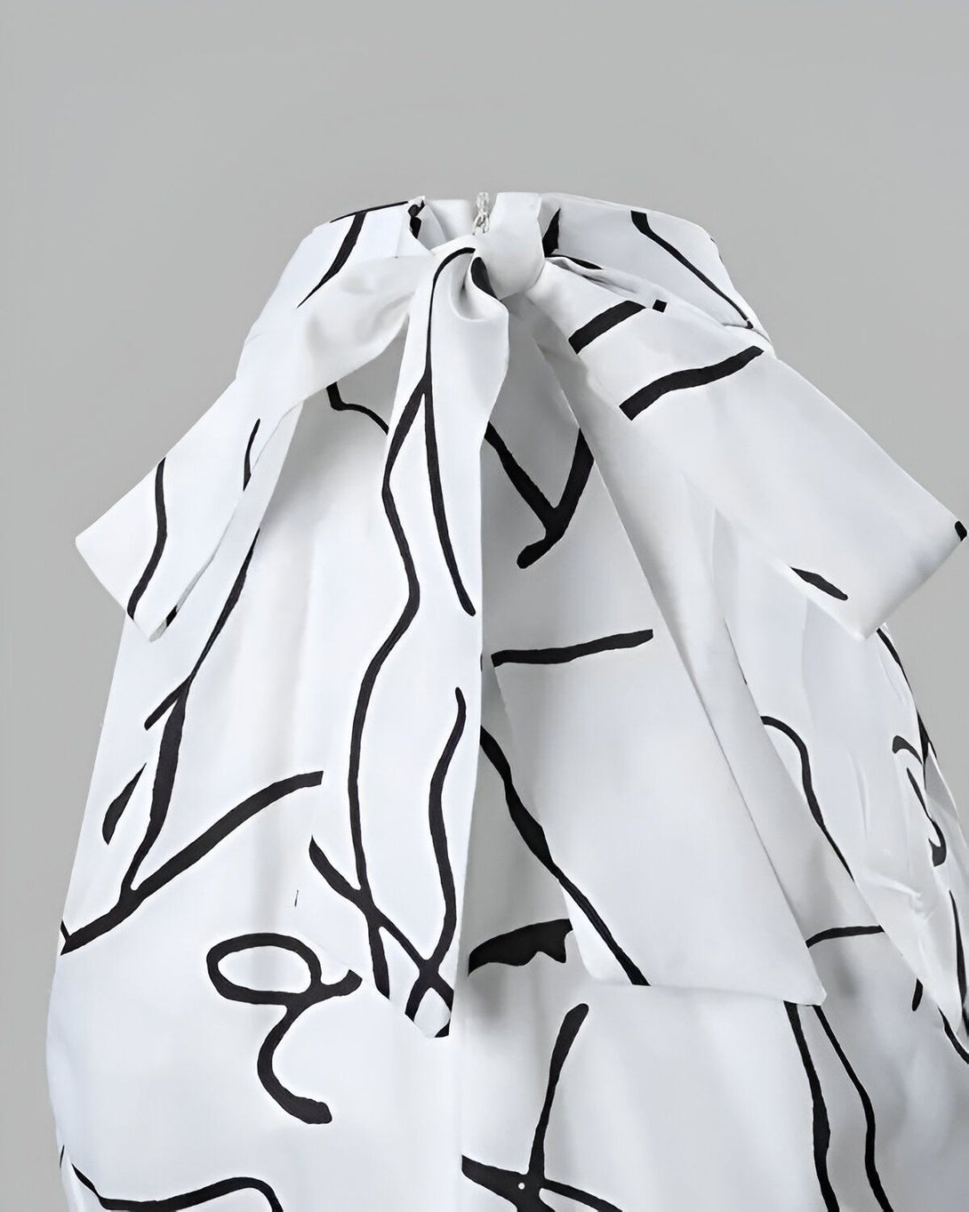 Une image d'une robe blanche avec un motif noir. La robe est nouée au niveau du cou et possède un col montant.