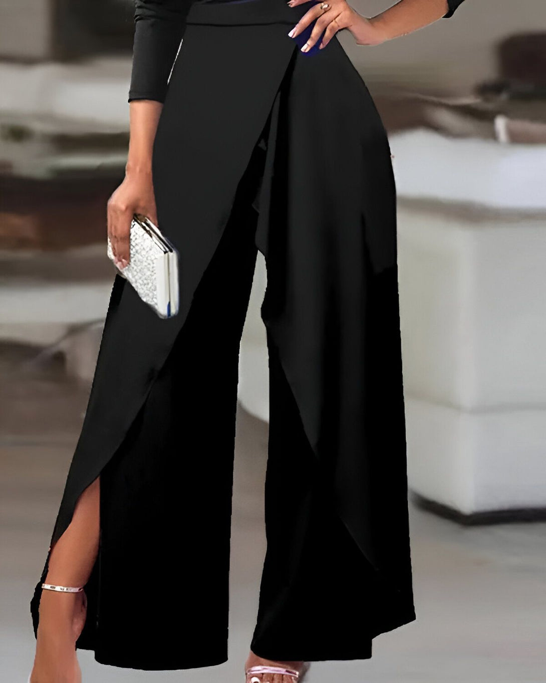 Une femme porte un pantalon taille haute noir avec une jambe évasée et une fente sur le côté. Elle porte également un haut noir à manches longues et des talons noirs.