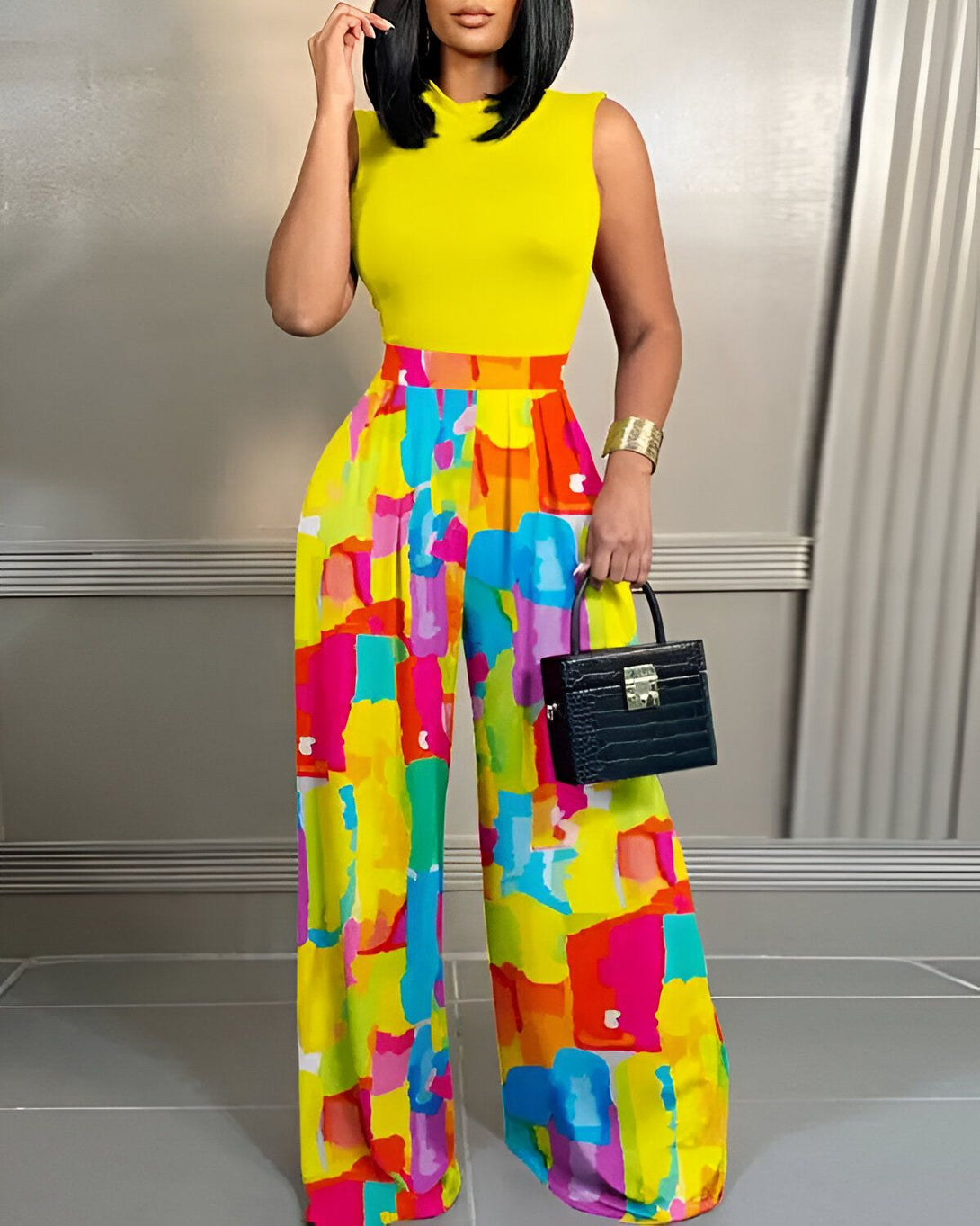 Une femme porte un pantalon large et coloré avec un haut jaune. Elle porte également un sac à main noir et des talons hauts.