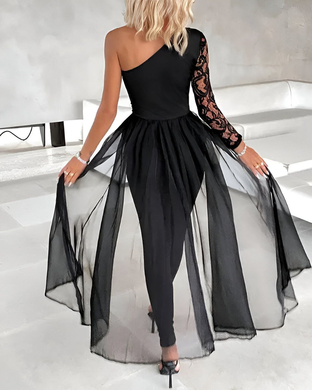 Une femme porte une combinaison noire avec une manche en dentelle et un pantalon évasé en mousseline de soie.