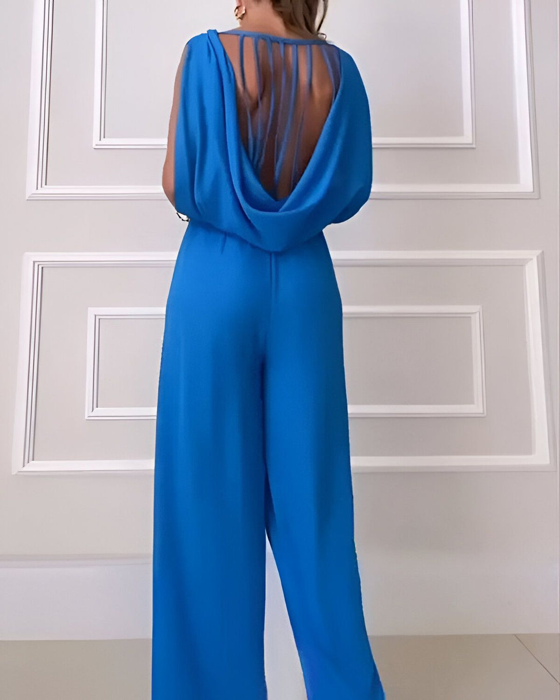 Une femme porte une combinaison pantalon bleu ciel. La combinaison a un dos nu avec un laçage.