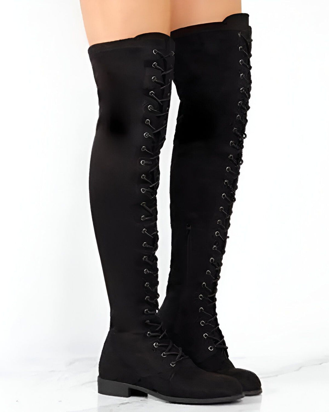 Une femme porte des bottes noires à lacets jusqu'aux genoux. Les bottes sont en daim et ont une semelle plate. La femme est debout sur un fond blanc.