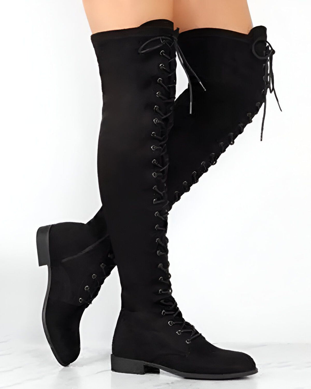 Une femme porte des bottes noires à lacets jusqu'aux genoux. Les bottes sont en daim et ont un talon épais. La femme est debout sur un fond blanc.