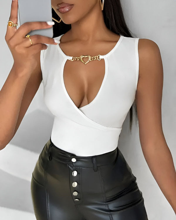 Une femme porte un body blanc avec un décolleté en cœur et une chaîne dorée. Elle porte également un pantalon en cuir noir.