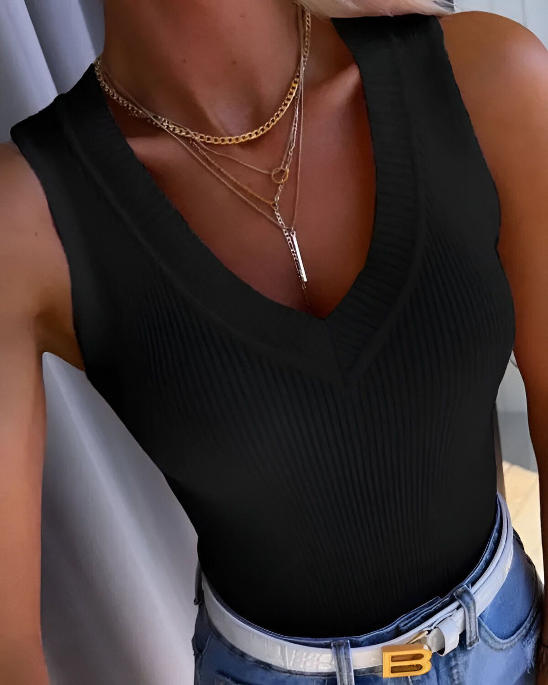 Une femme porte un débardeur noir avec un col en V profond. Elle porte également plusieurs colliers et un jean bleu.