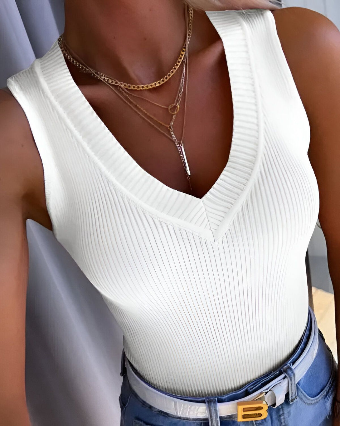 Une jeune femme porte un débardeur côtelé blanc et un jean bleu. Elle porte également plusieurs colliers.
