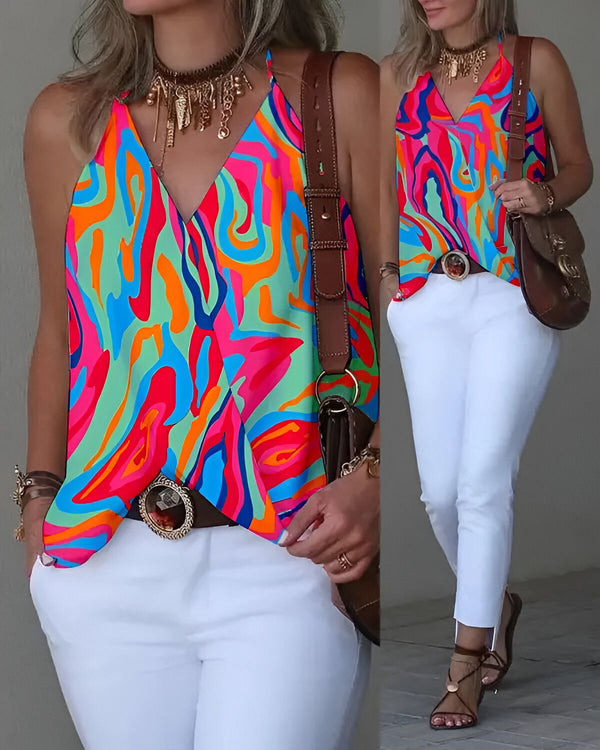 Une femme porte un haut coloré et un pantalon blanc. Elle a un collier, une ceinture et un sac à main marron. Elle porte des sandales marron clair.