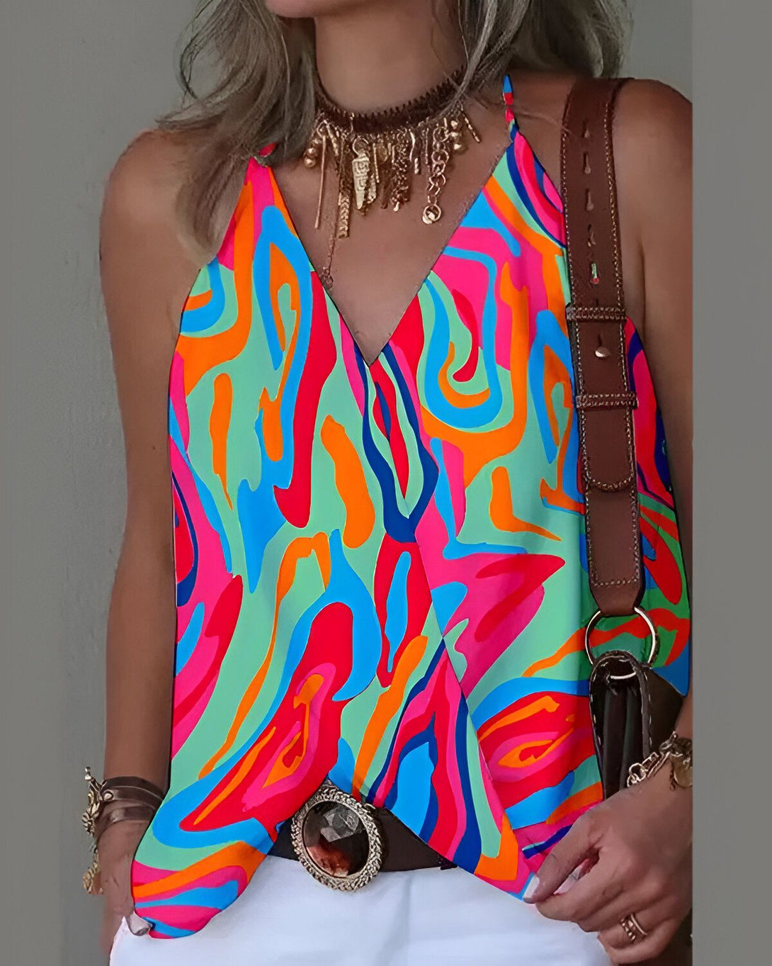 Une femme porte un débardeur coloré avec un motif tie-dye. Le débardeur est orange, rose et bleu. La femme porte également un collier et un sac à main marron.