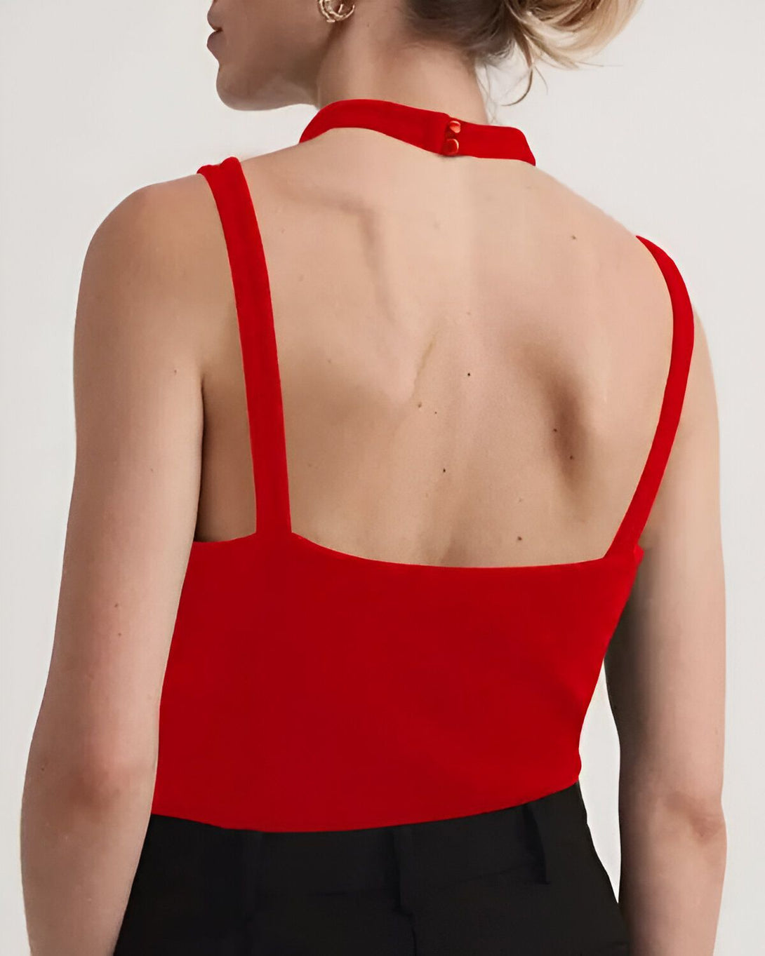 Une femme porte un haut rouge dos nu. Le haut est court et ajusté, avec des bretelles fines.
