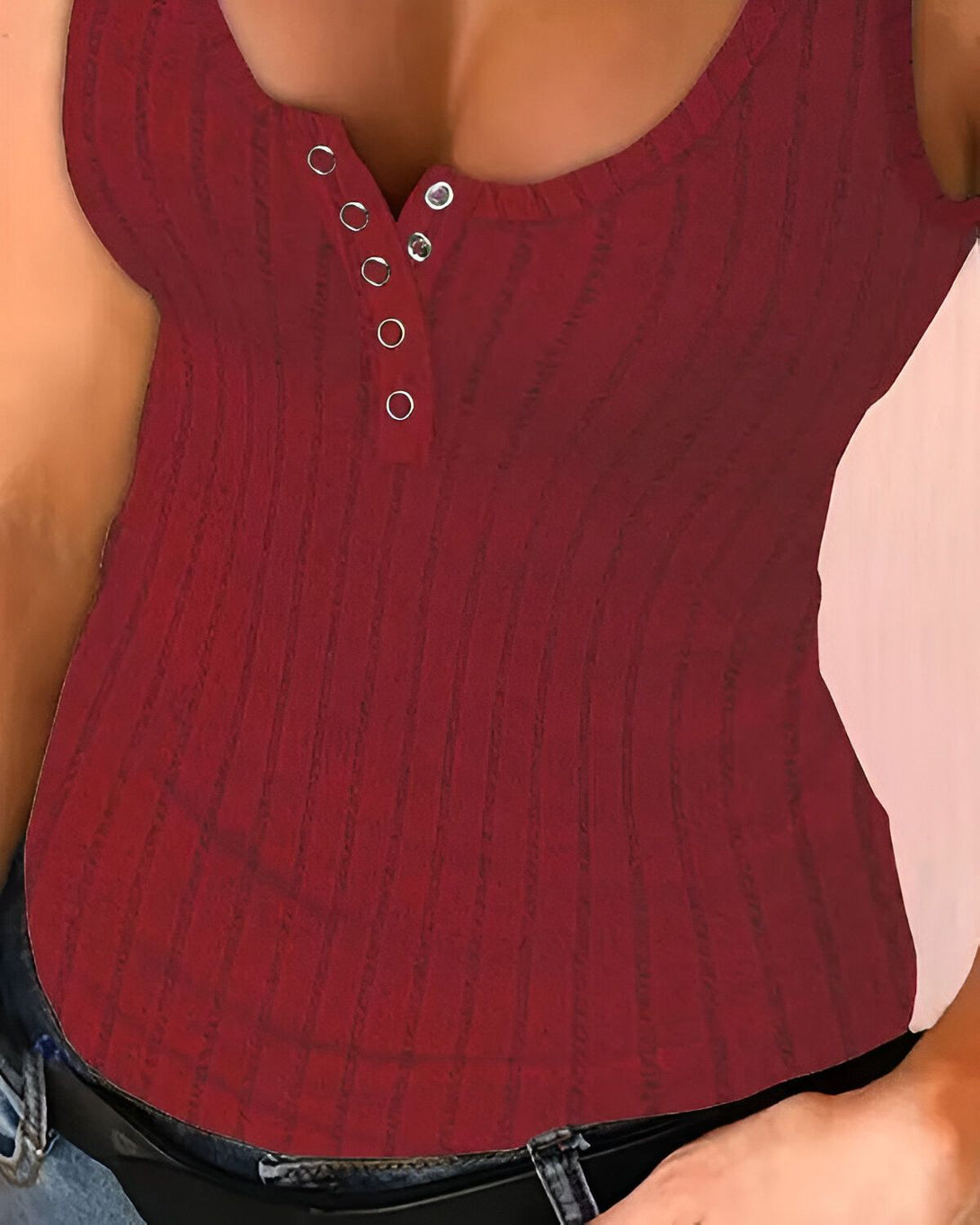 Une femme porte un débardeur côtelé rouge. Le débardeur est cintré et a des boutons sur le devant. La femme porte également un jean bleu.