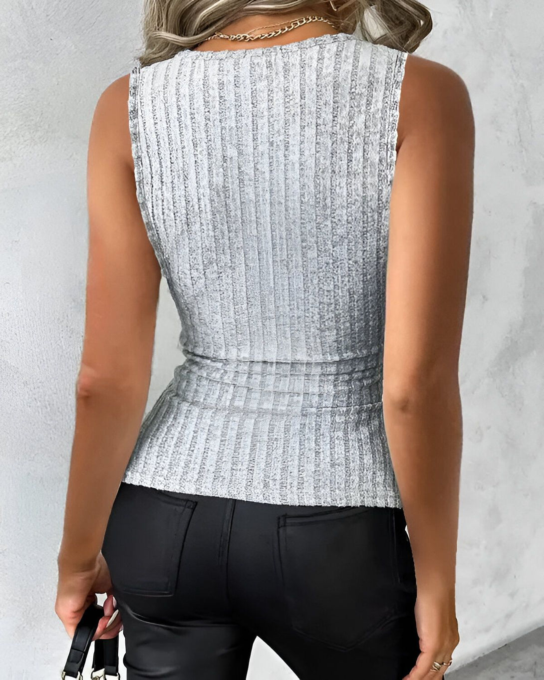 Une femme porte un débardeur côtelé gris et un pantalon en cuir noir.