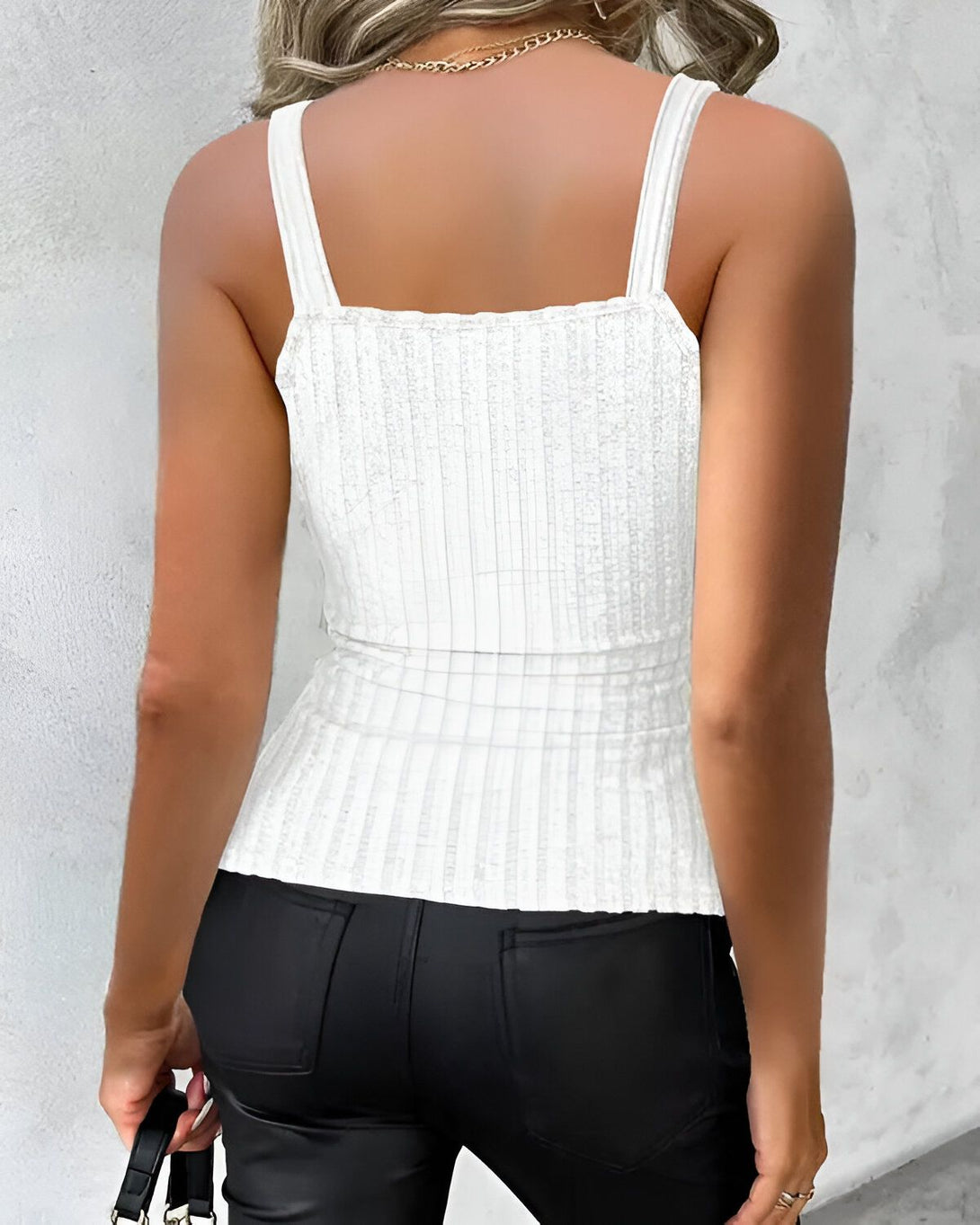 Une femme porte un débardeur côtelé blanc et un pantalon en cuir noir.