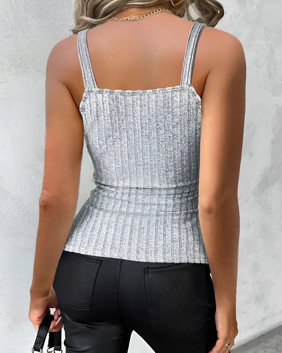 Une femme porte un débardeur côtelé gris et un pantalon en cuir noir.