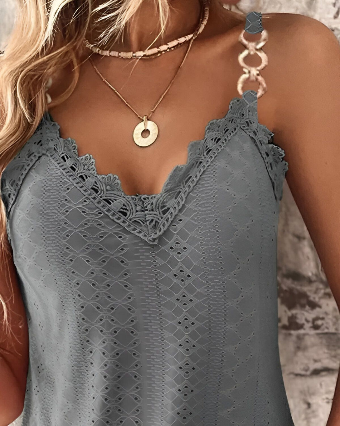 Une femme porte un débardeur gris en dentelle avec un collier.