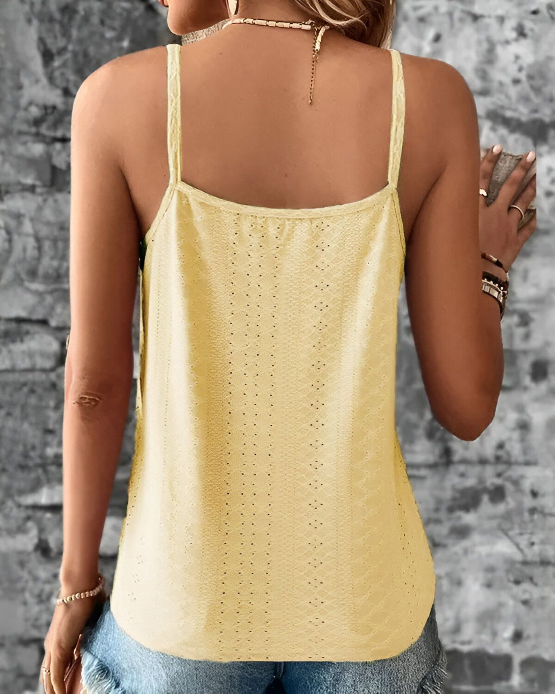 Une femme porte un débardeur jaune dos nu. Le débardeur est en crochet et a des bretelles fines. La femme est vue de dos et porte un jean bleu.